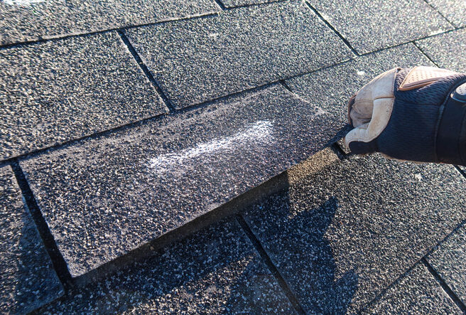 A member of Abe’s Roofing & Exteriors lifts a damaged shingle, which is a sign of needing roof repair. Roofers Chatham IL
