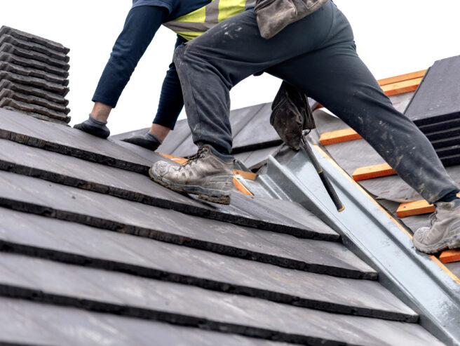Construction worker carefully places roof tiles on a sloped surface while standing on top of a building showcasing the effort involved in roof replacement