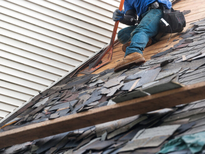 Roofers in Jacksonville IL remove old asphalt roof shingles with roofing removal tool from suburban home for replacement of new roof tiles.